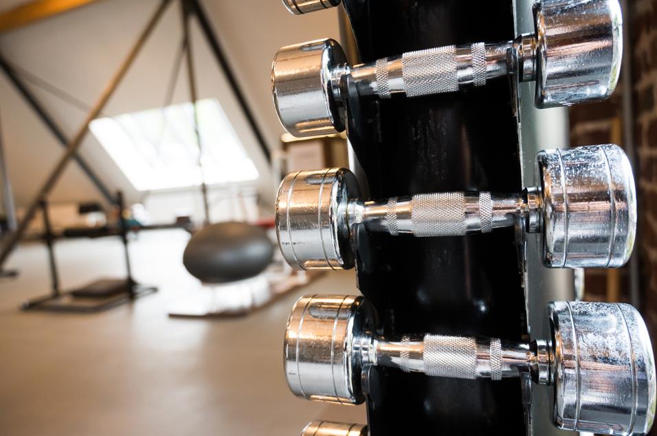 Nahaufnahme von mehreren chromierten Hanteln an einem Ständer in einem modernen Fitnessstudio.