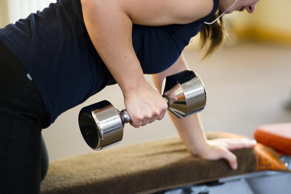 Frau macht eine Bizepsübung mit einer Hantel, während sie auf einer Trainingsbank lehnt.