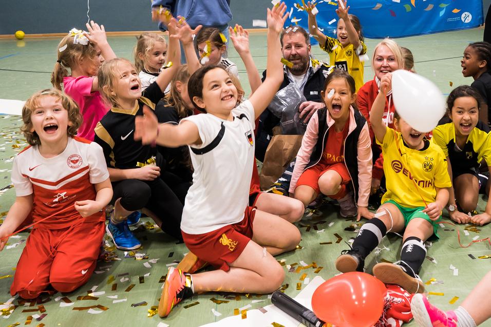 Gruppenszenen mit begeisterten Kindern in Sportkleidung, die Ballons halten und vor einem Danke-Schild feiern.