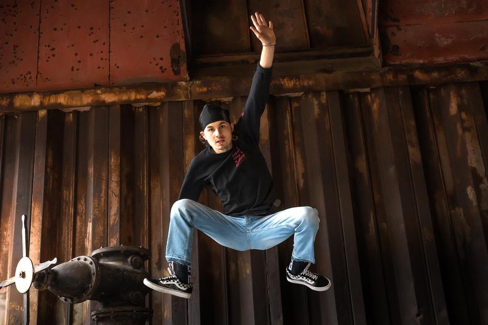 Junger Mann springt lässig von einer Metallstruktur auf ein schwarz-weiß kariertes Muster.